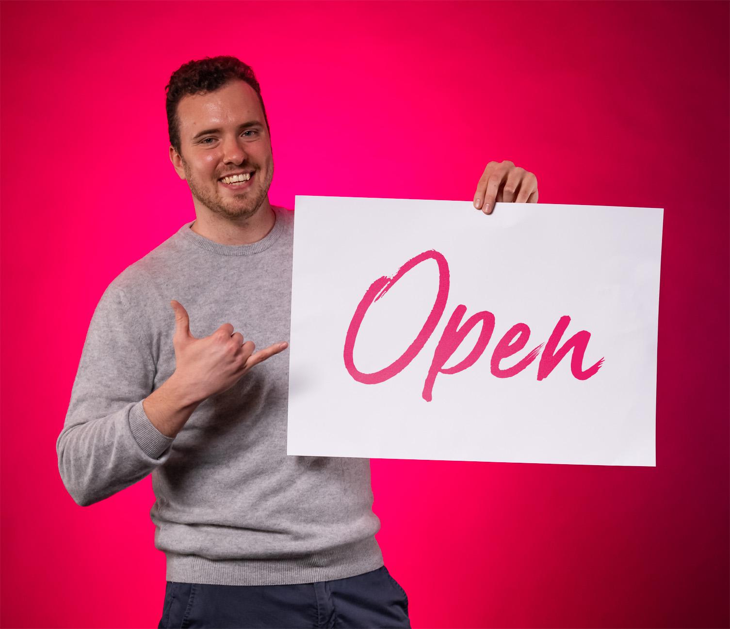 BE-terna employee holding “Open” sign promoting job openings and open company culture in IT careers.